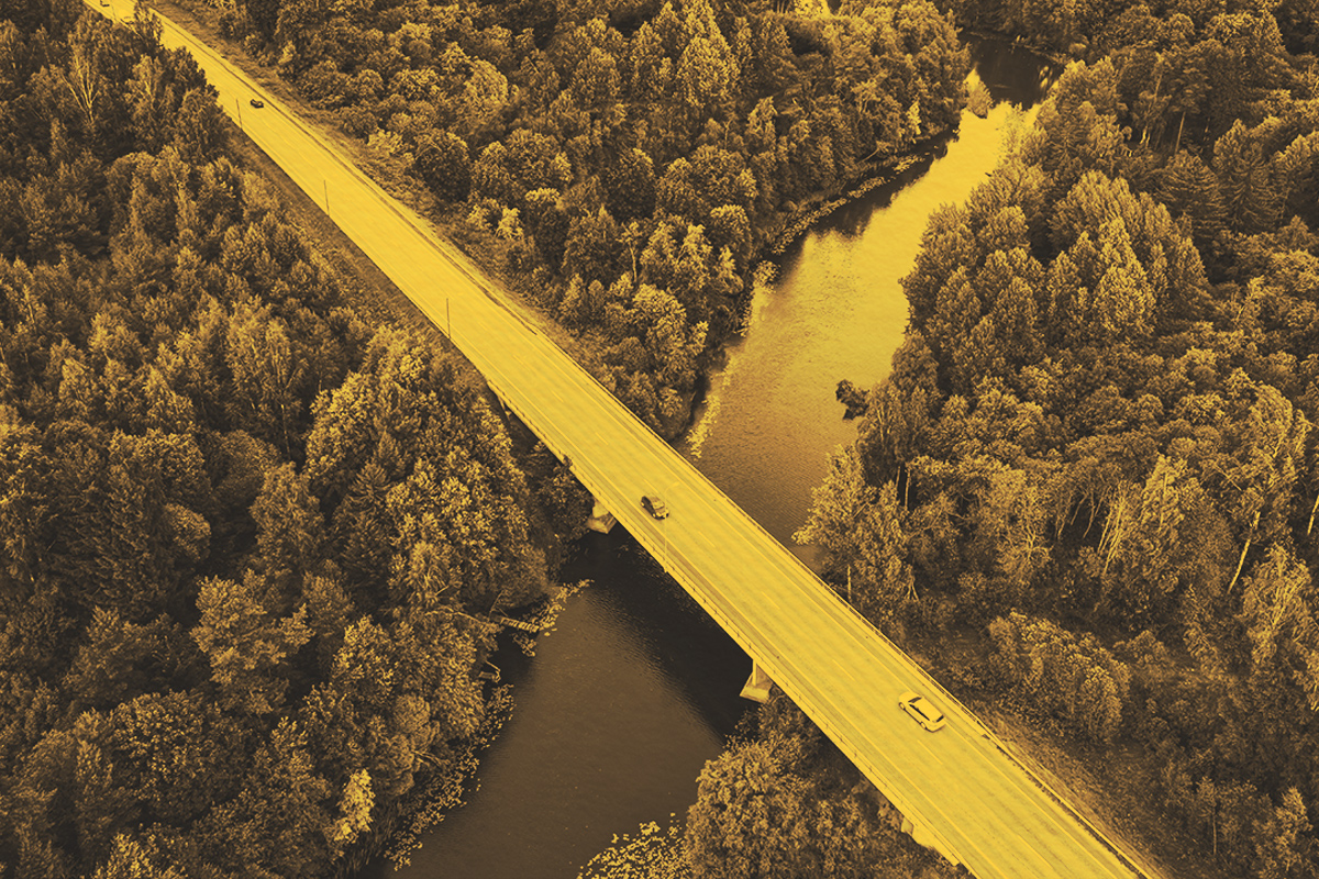Aerial view of asphalt road with cars over blue river and green woods
