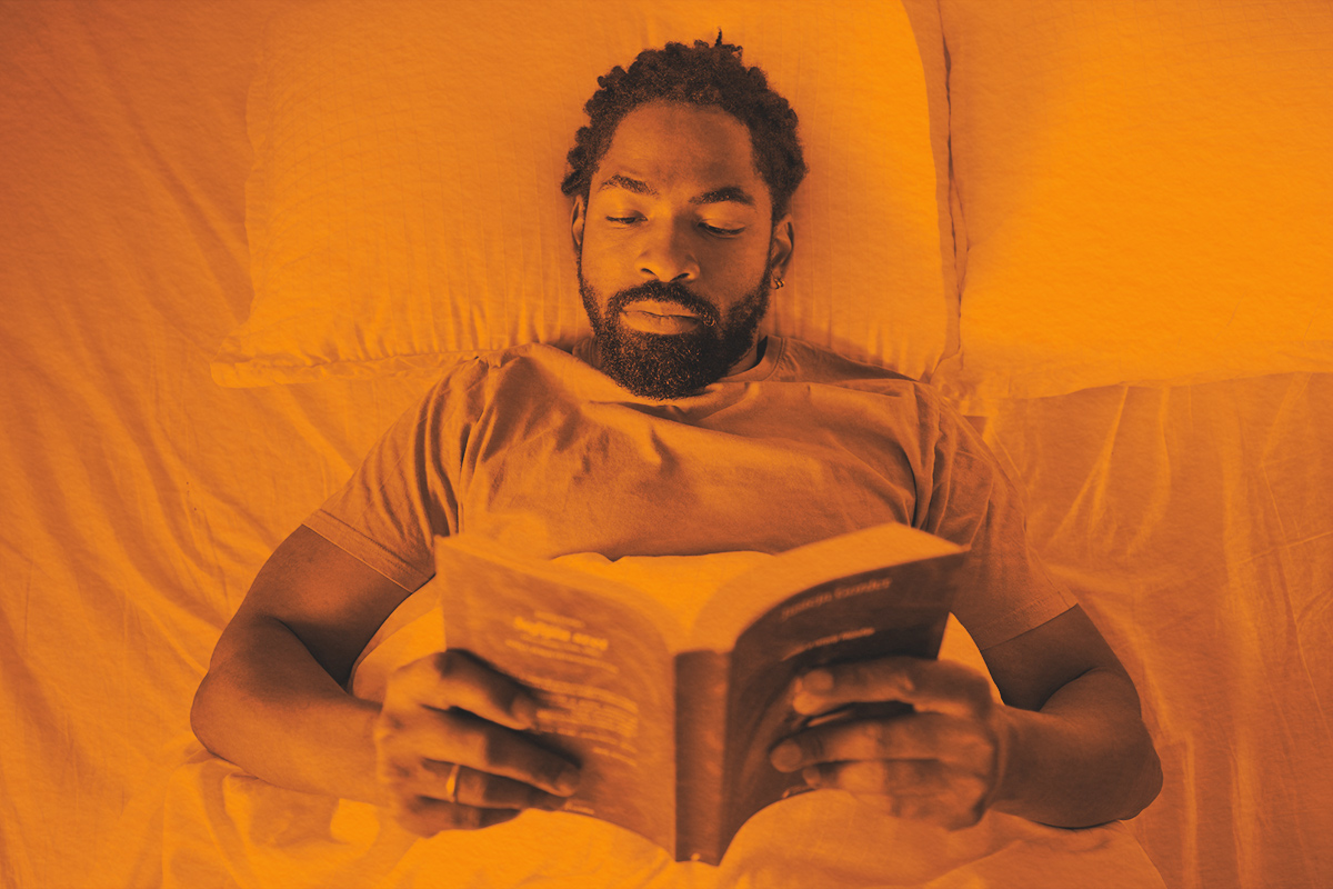 High angle view of man reading a book while relaxing in bed