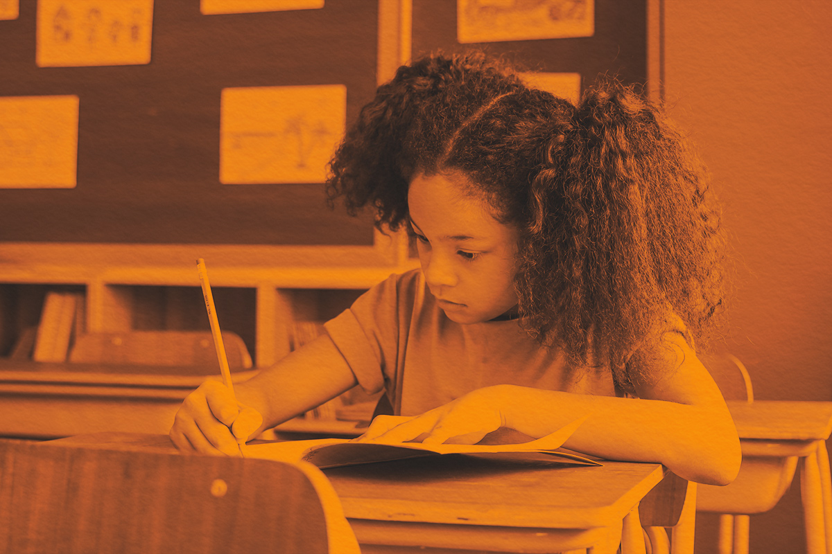 girl sitting in classroom writing in book with pencil