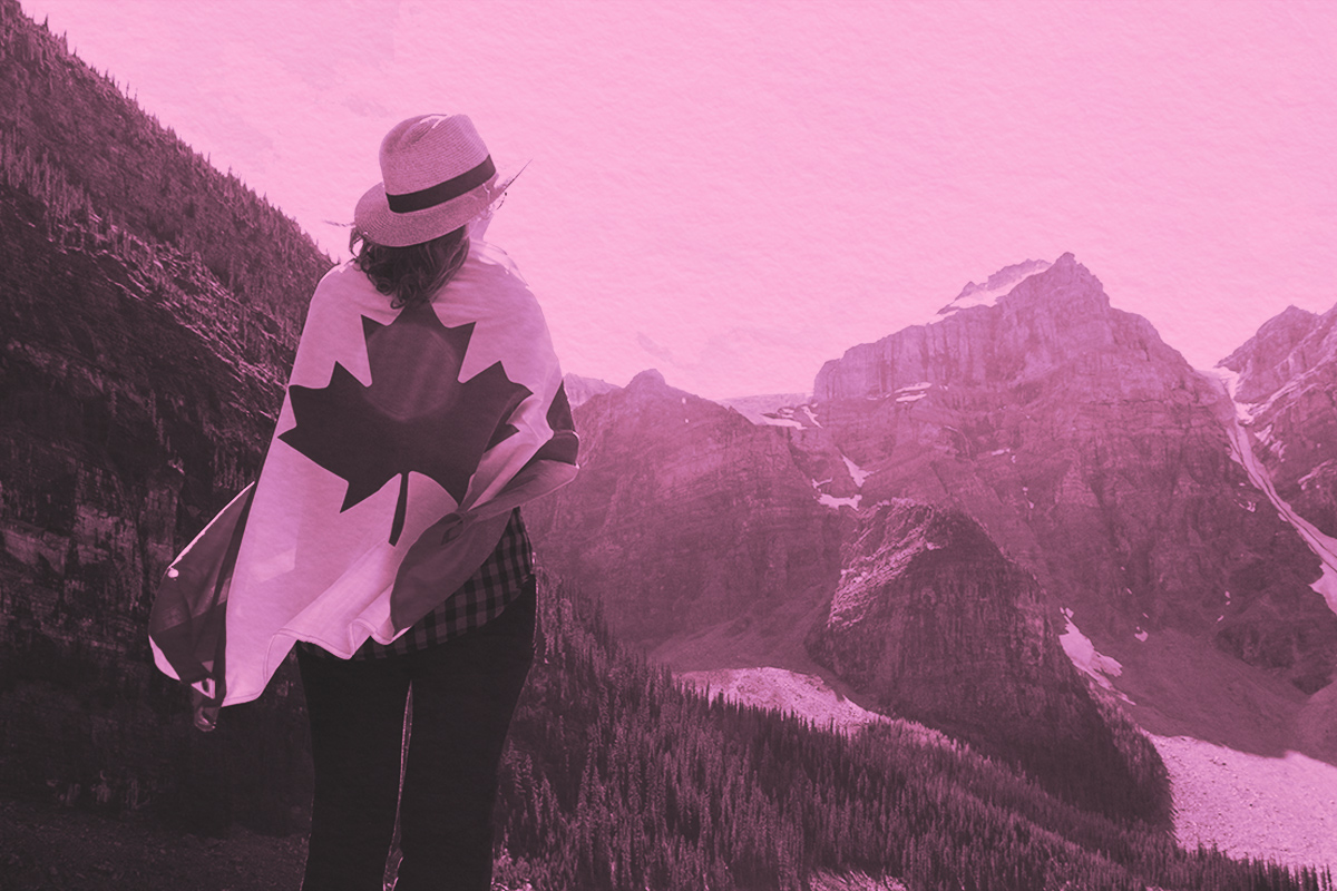 Woman with Canadian flag wrapped around her, looking towards the Canadian mountains