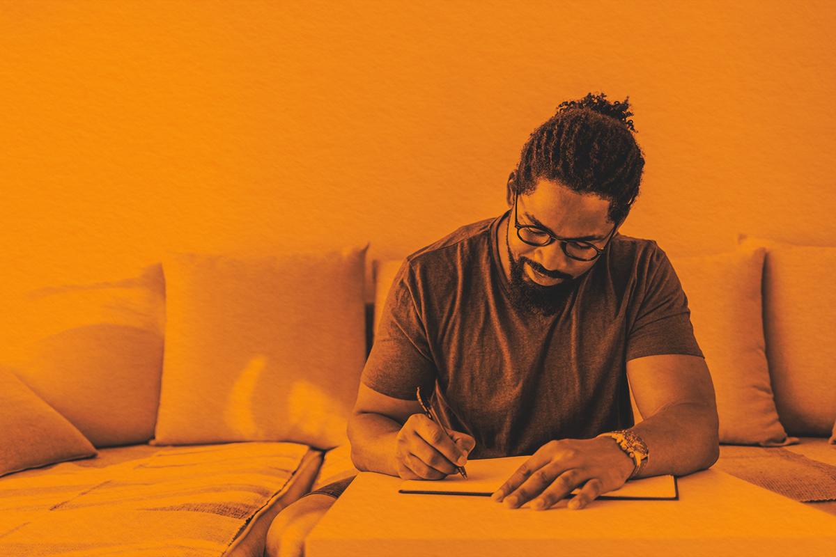Man sitting on couch, writing in notebook