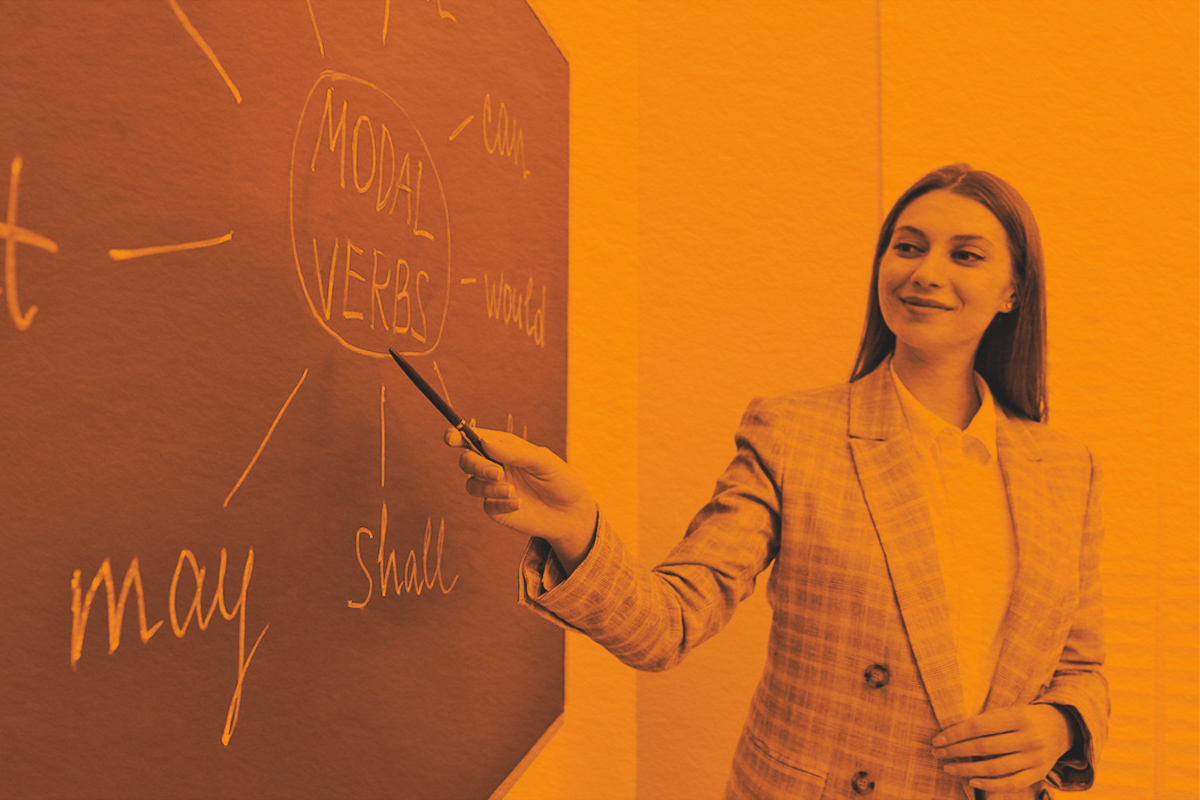 English teacher giving lesson on modal verbs on a classroom chalkboard