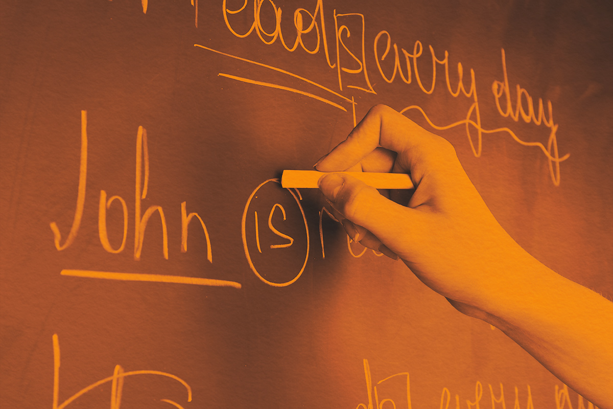 Teacher hand writing grammar sentences on board with chalk