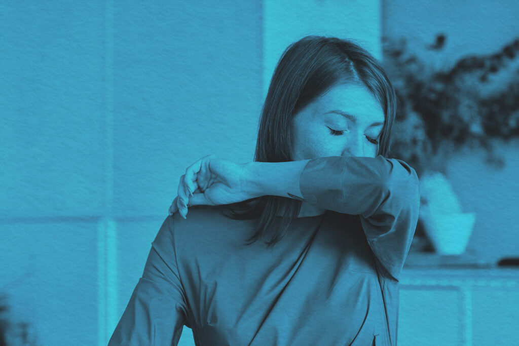 Woman covers mouth sneezing in office setting