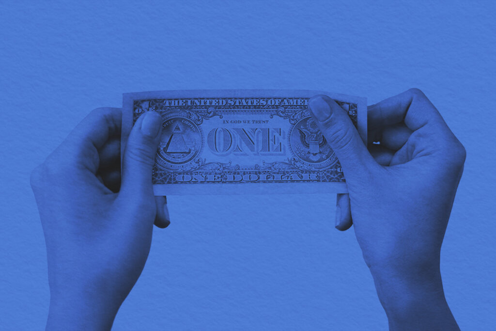 A close-up image of hands holding a one dollar bill